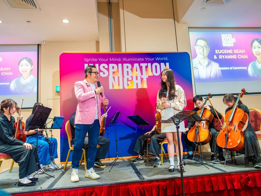 Eugene Seah emceeing Inspiration Night with a student orchestra on stage